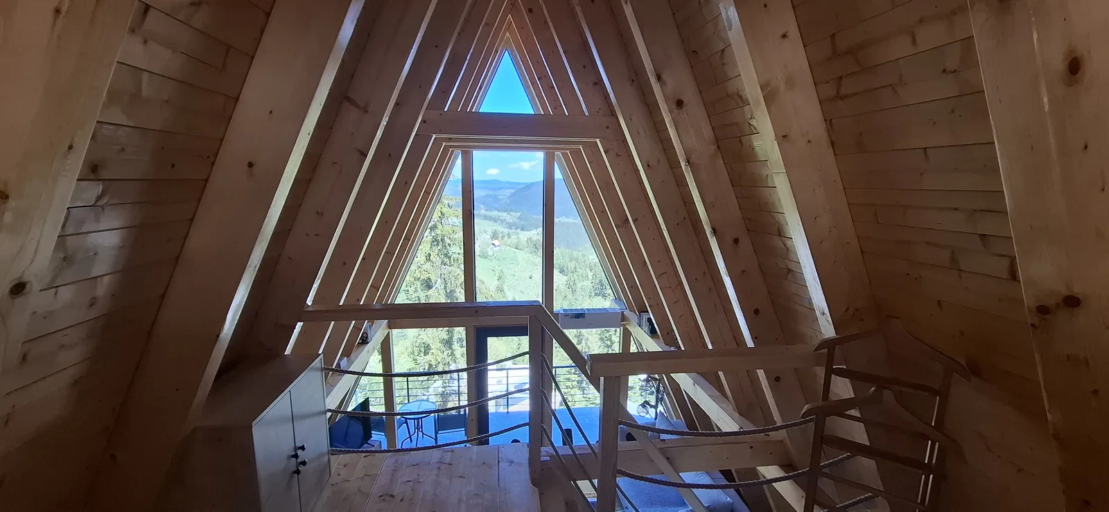 Pogled sa mezanina kroz veliki trougaoni stakleni zabat A-frame kuće.