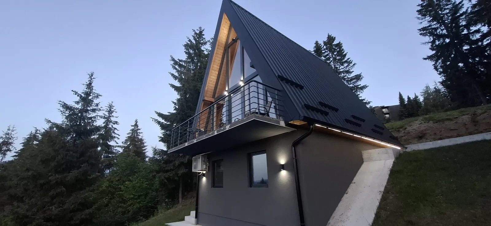 A-frame vikendica u plavi sat sa toplo osvetljenim strehama i pogledom na planine.